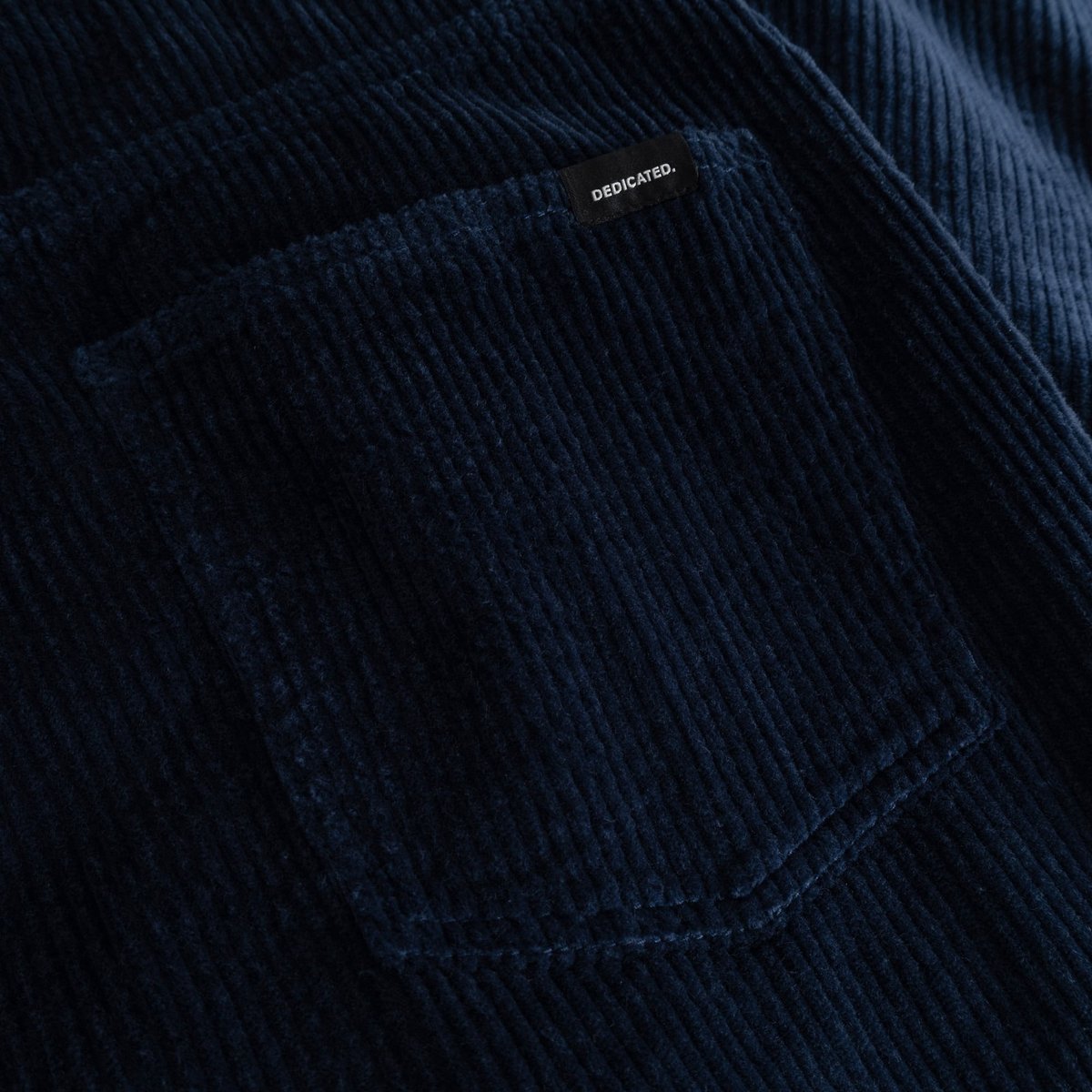 A detailed shot of the rich navy corduroy fabric on the Hamburg pants, with the Dedicated label on the back pocket.