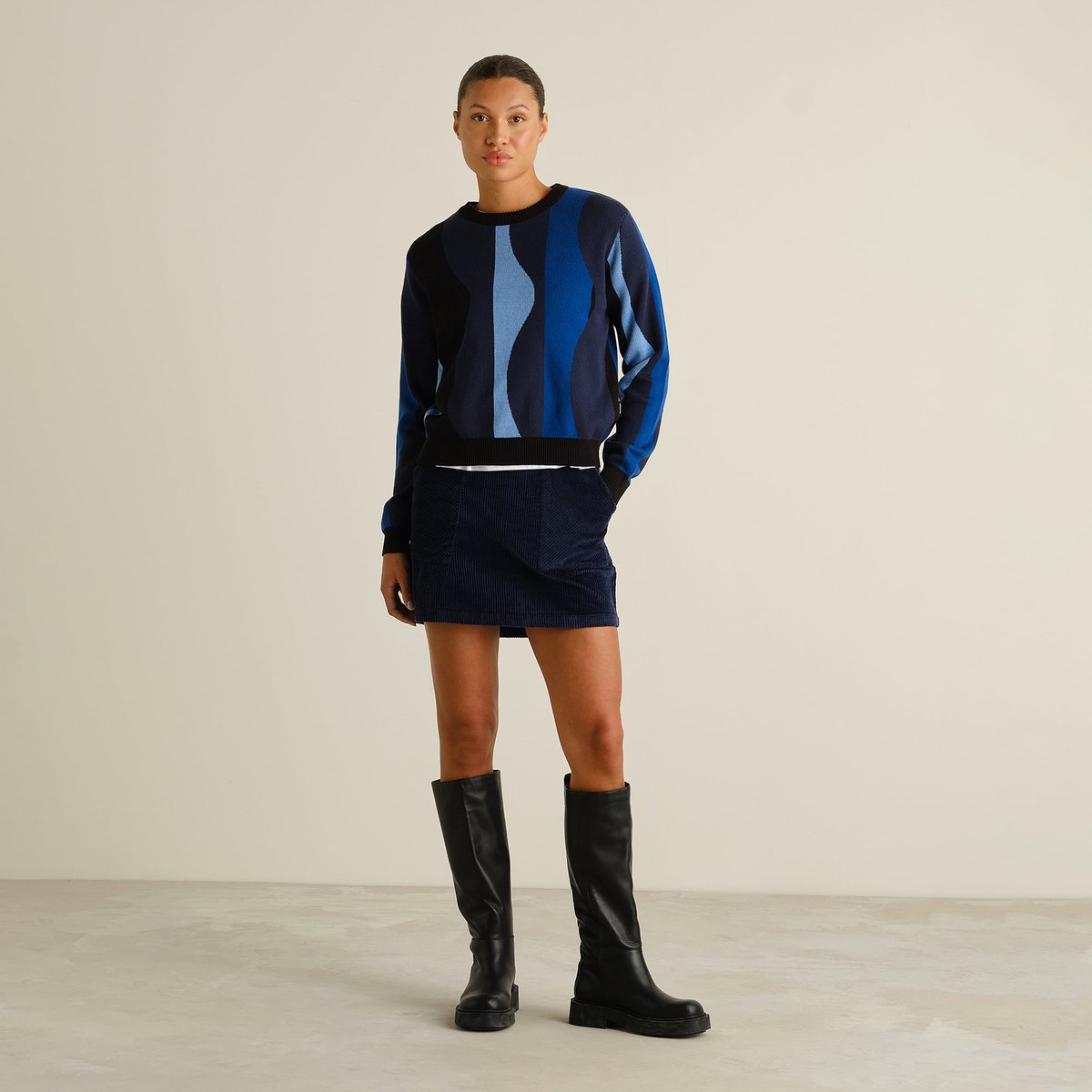 Full length view of a model wearing the Sweater Arendal Wavy Stripe Blue with a navy mini skirt and black boots.