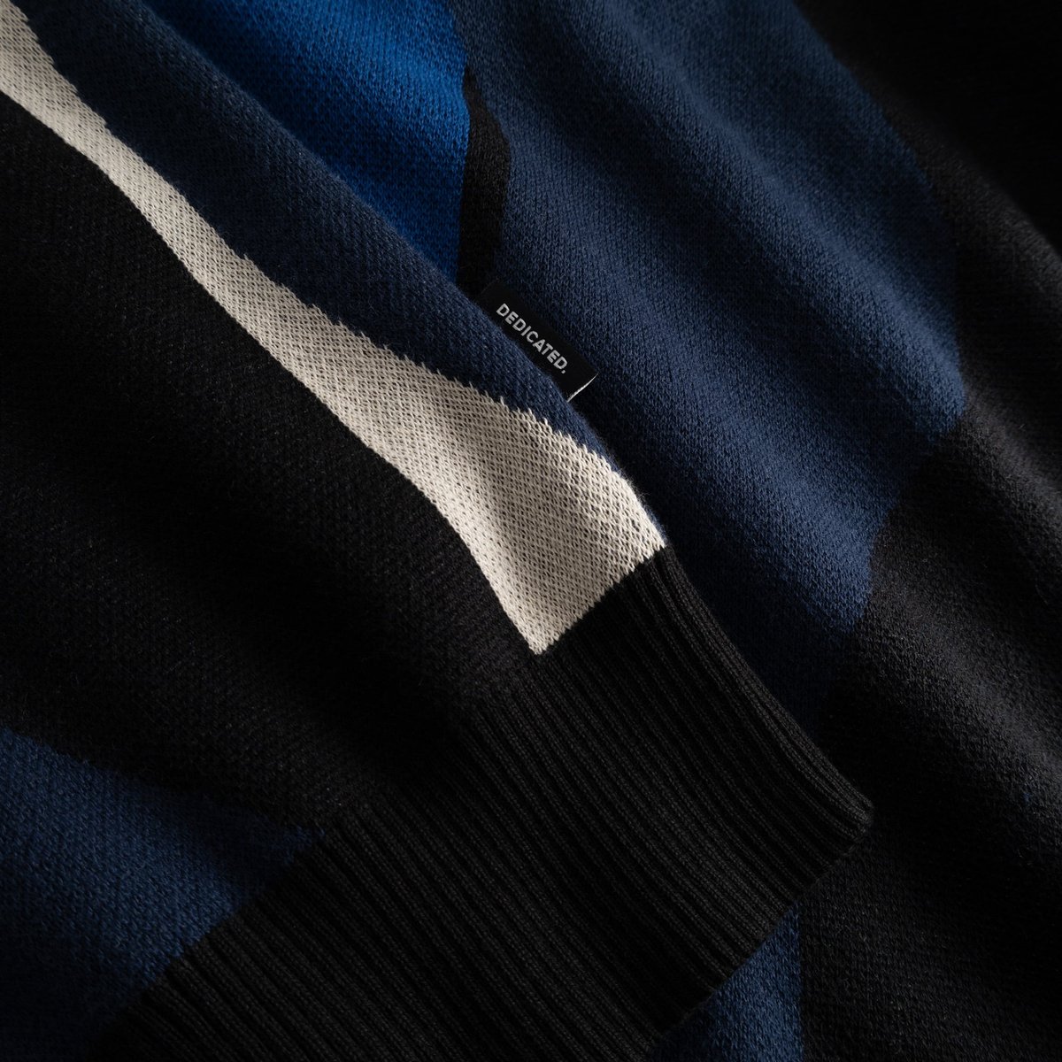 A close-up of the Sweater Mora Wavy Stripe Blue, highlighting the intricate jacquard knit, ribbed cuff, and brand label.