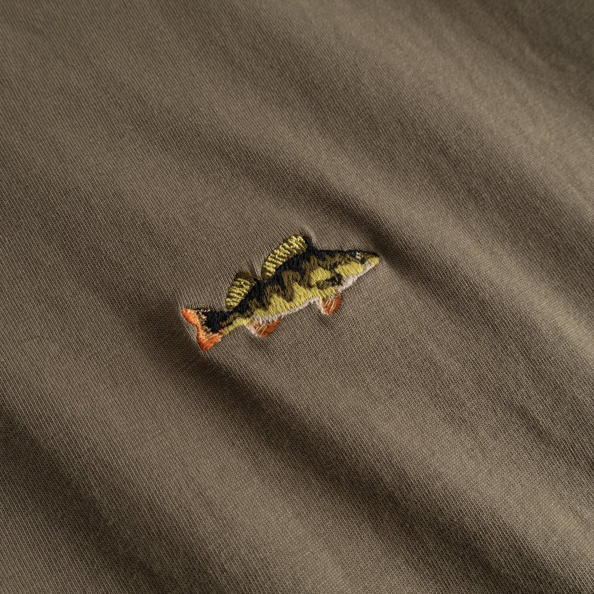A detailed close-up of the perch fish embroidery on the T-shirt Stockholm in Bungee Green.