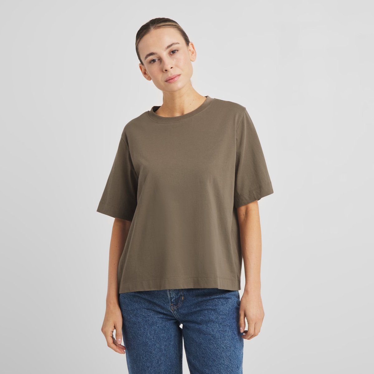 Front view of a woman wearing the T-shirt Vadstena Base in Bungee Green with a pair of classic blue jeans.
