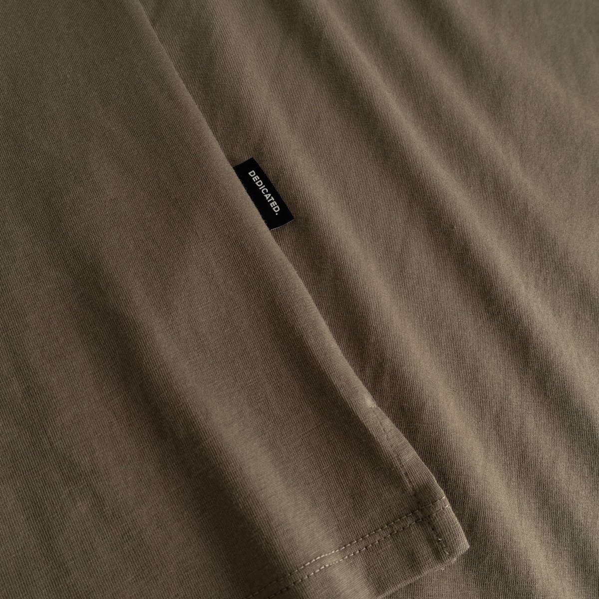 Detailed shot of the soft, bungee green fabric of the Visby T-shirt, with the classic Dedicated label on the side seam.