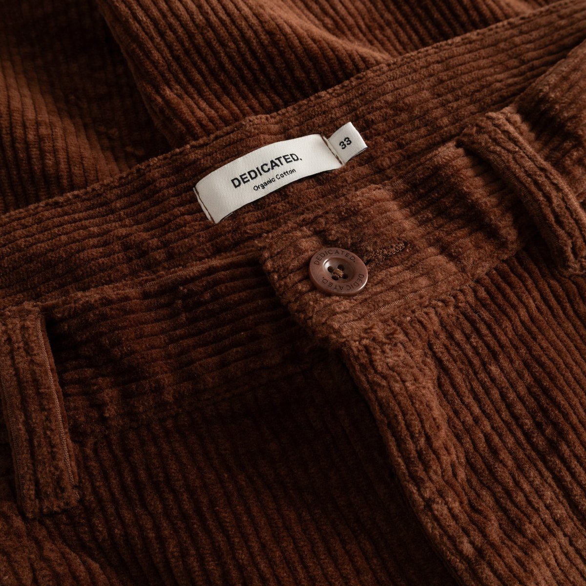 A close-up of the brown corduroy fabric on the Pants Hamburg, showing the DEDICATED brand label at the waistband.