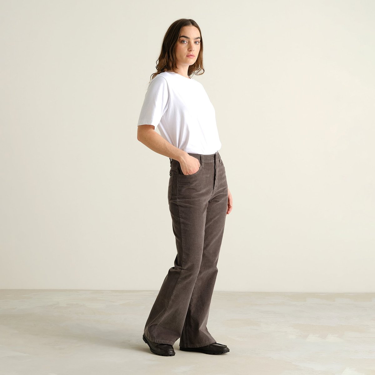 Ein Model trägt die Bootcut-Cordhose Ryda in Rock Grey und ein schlichtes weißes T-Shirt.