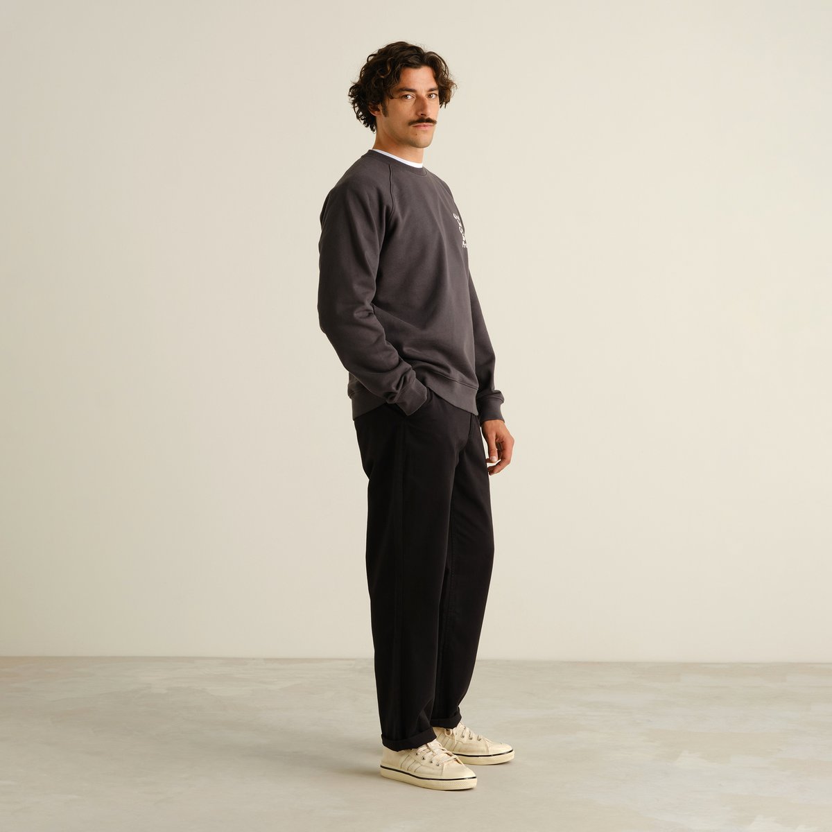 A model wears the black Chino Pants Hudiksvall, styled with a grey sweatshirt and sneakers for a relaxed, polished look.