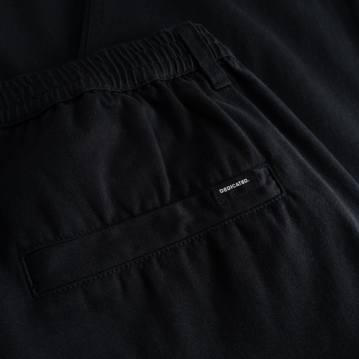 A detailed look at the comfy elastic waistband and back welt pocket of the black Hudiksvall Chino Pants.