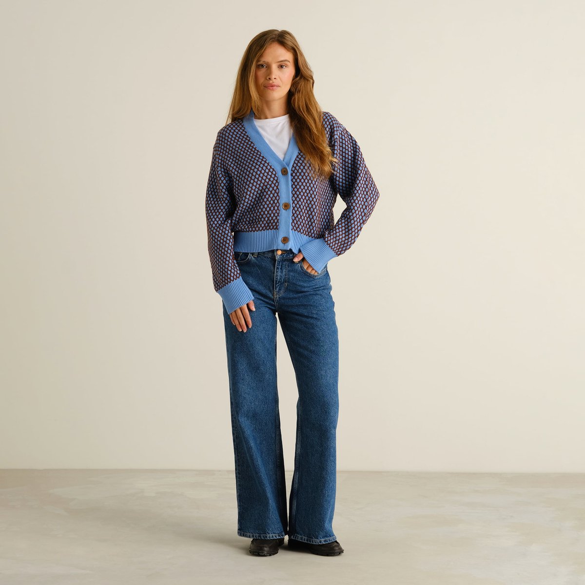 Kvinna i den blå och bruna stickade koftan Kanan Bubble Knit, stylad med klassiska jeans med vida ben.