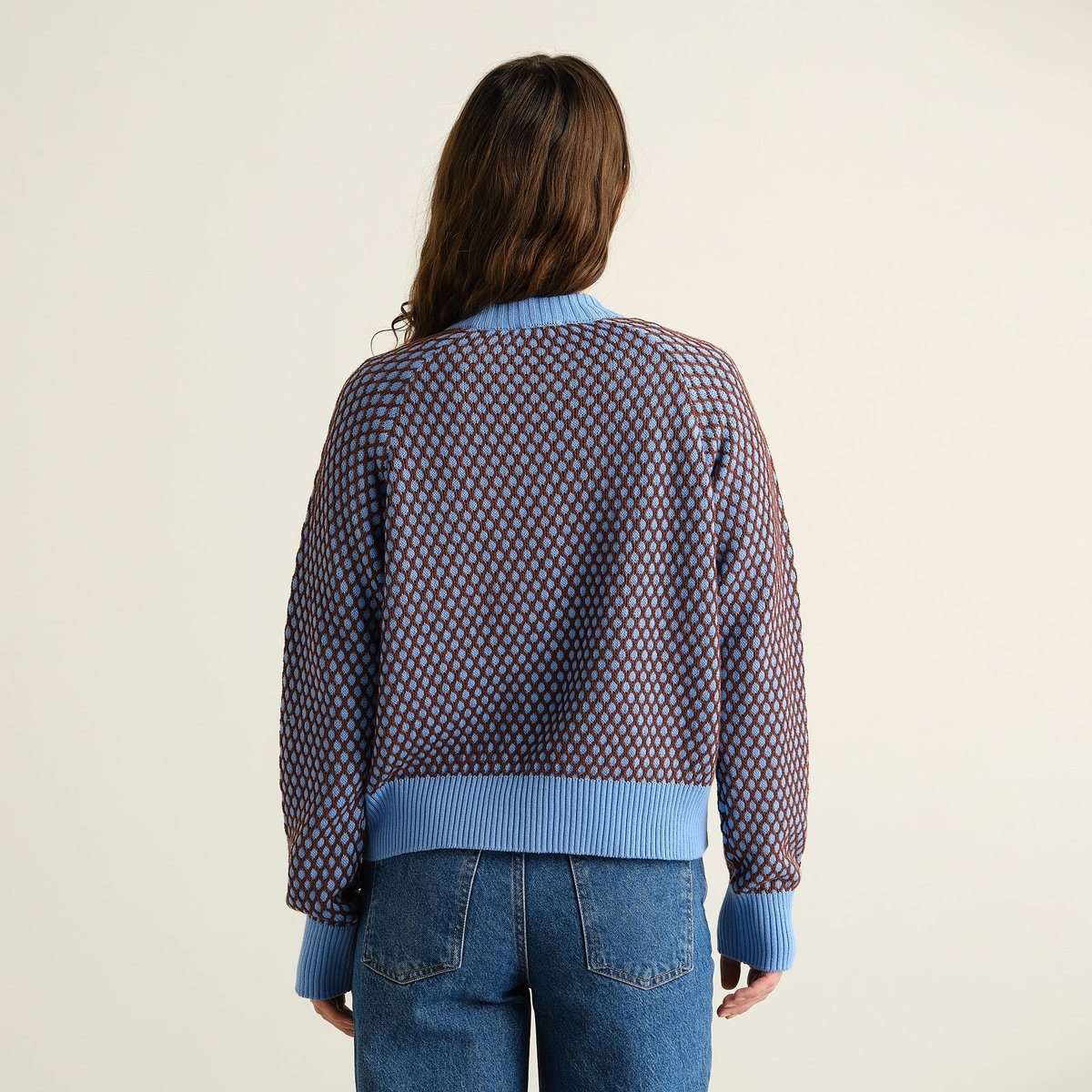 Baksidan av en kvinna som bär den stickade tröjan Husie Bubble Knit i blått och brunt med blå jeans.