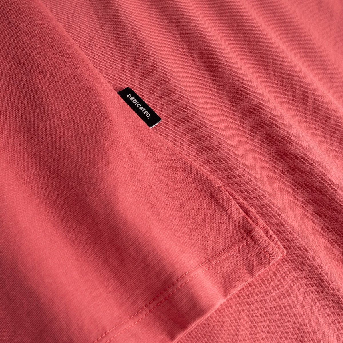 Close-up detail of the Visby T-shirt in Holly Red, showing the side slit and the subtle Dedicated brand tab.
