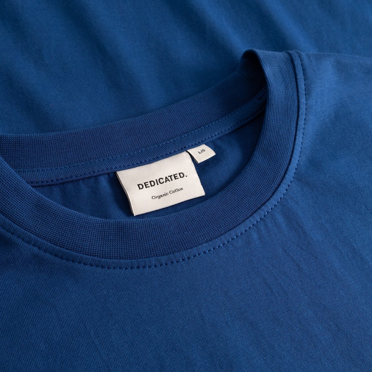 Närbild på T-shirt Stockholm Base i Limoges Blue, som visar den ribbade halsringningen och Dedicateds märkning.