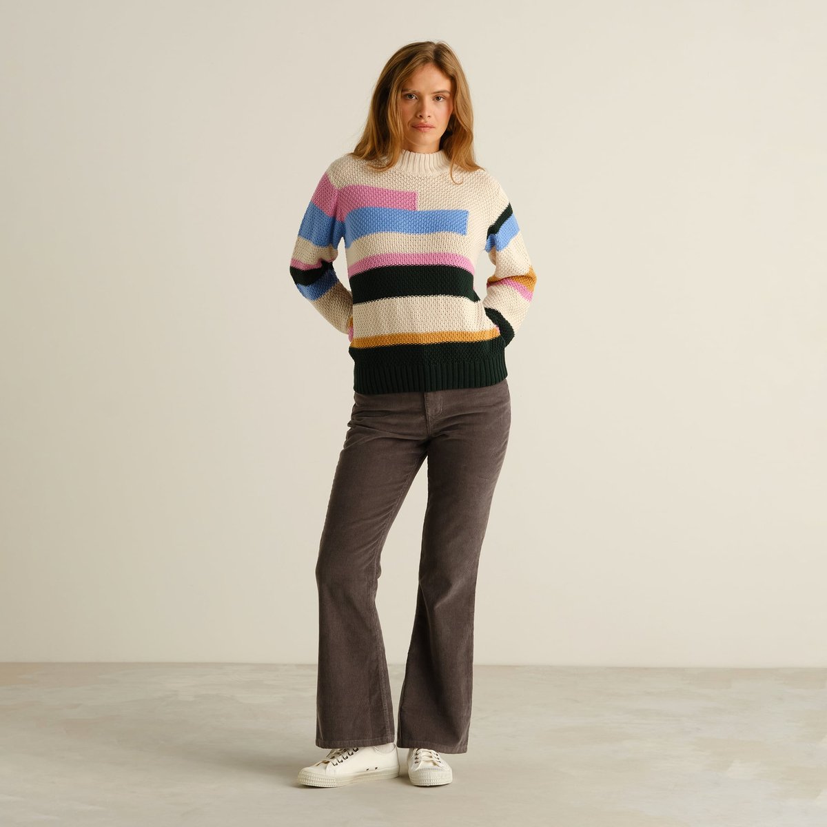 Full view of a model wearing the cozy Sweater Gotland in a fun multi-color stripe pattern with brown flared corduroys.