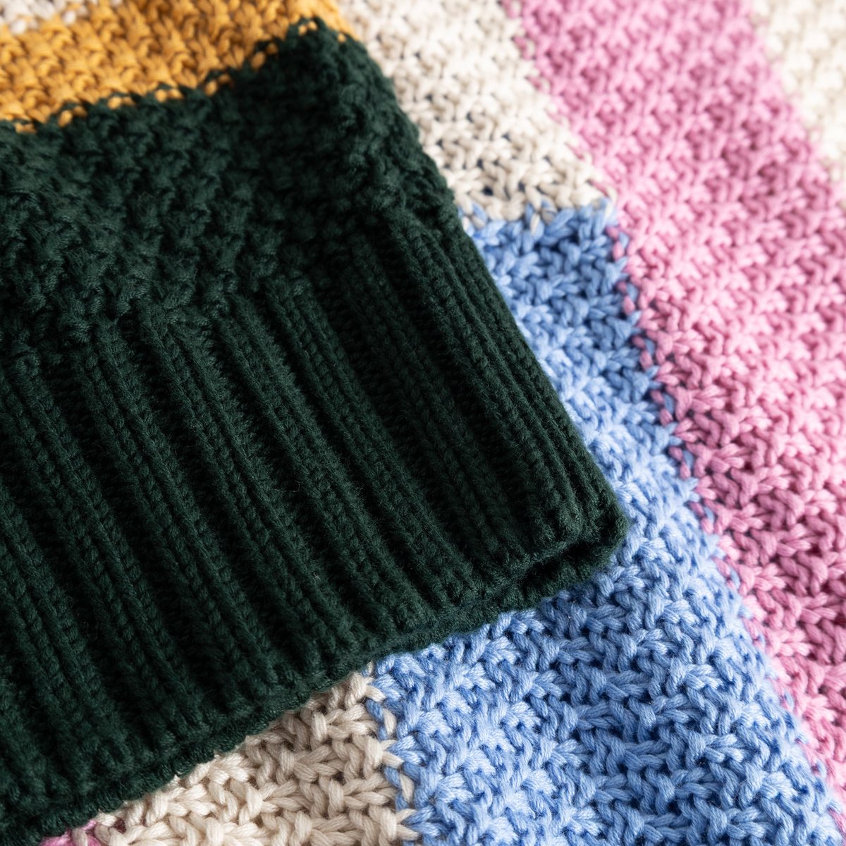 A close-up of the cozy, chunky knit of the Gotland sweater, highlighting the dark green ribbed collar and colorful stripes.