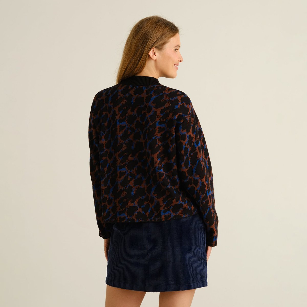 A woman looks over her shoulder, showing off the back of the cozy Limhamn sweater in a cool multi-colored leopard print.