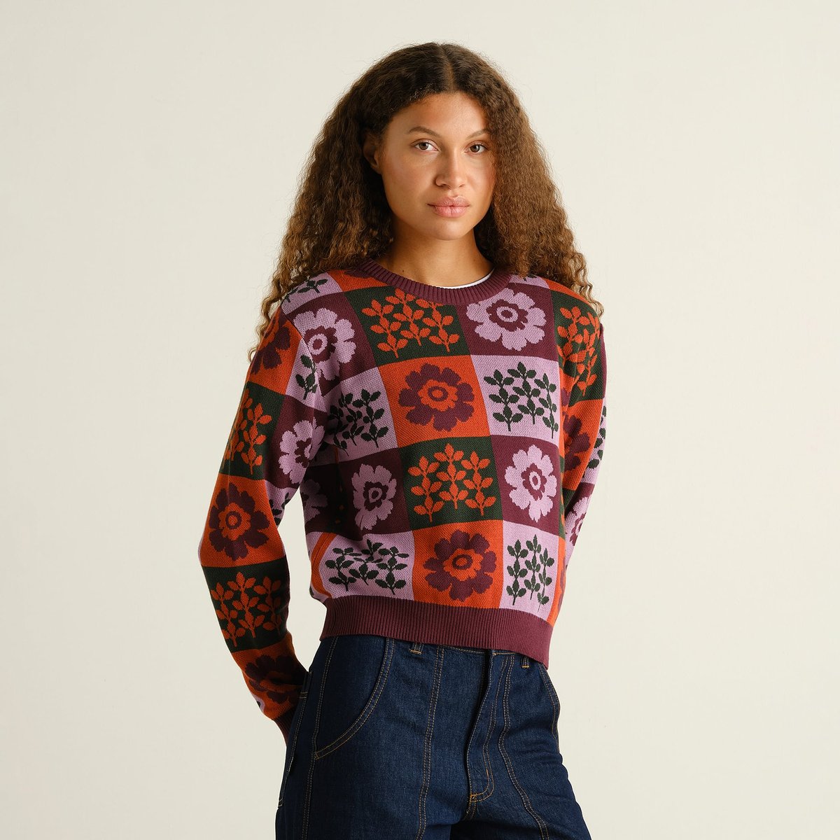 Model wears the Arendal Nature Check sweater, a cozy jacquard knit with a multi-colored floral and leaf checkerboard pattern.