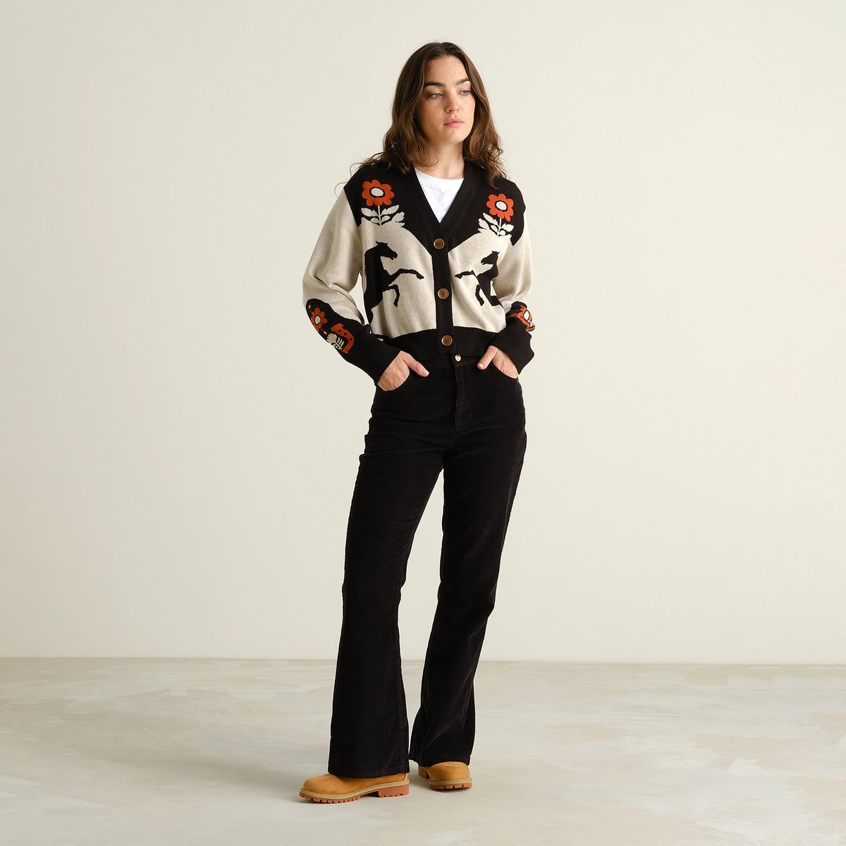 Full length shot of a woman wearing the Kanan Western Multi Color cardigan, paired with black flared trousers and tan boots.