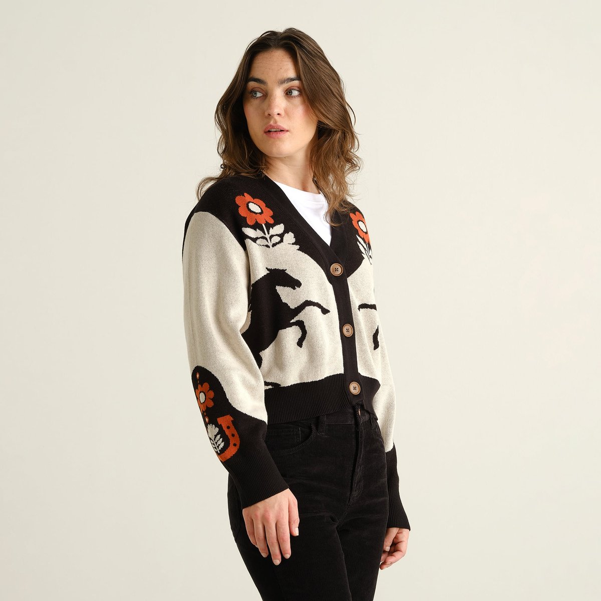 A woman looks over her shoulder wearing the Kanan Western cardigan in a multi-color pattern with black trousers.