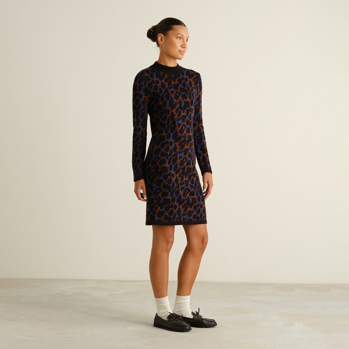 Seitenansicht eines Models, das das Strickkleid Lo Leopard Multi Color zu Loafern und weißen Socken trägt.