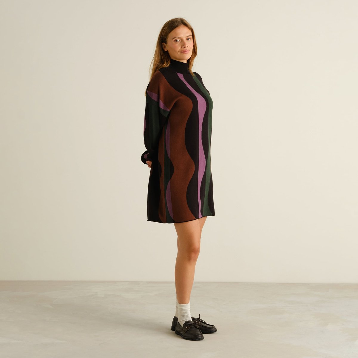 Side view of a woman wearing the loose-fit knitted Nikkala dress in a playful wavy stripe pattern.