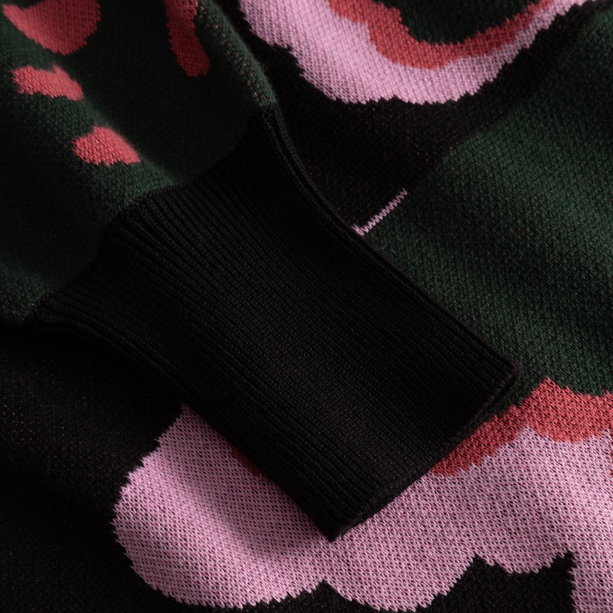 Nahaufnahme des weichen Jacquardstricks des Kleides Nikkala mit schwarzem Rippbündchen und buntem Big-Bloom-Muster.