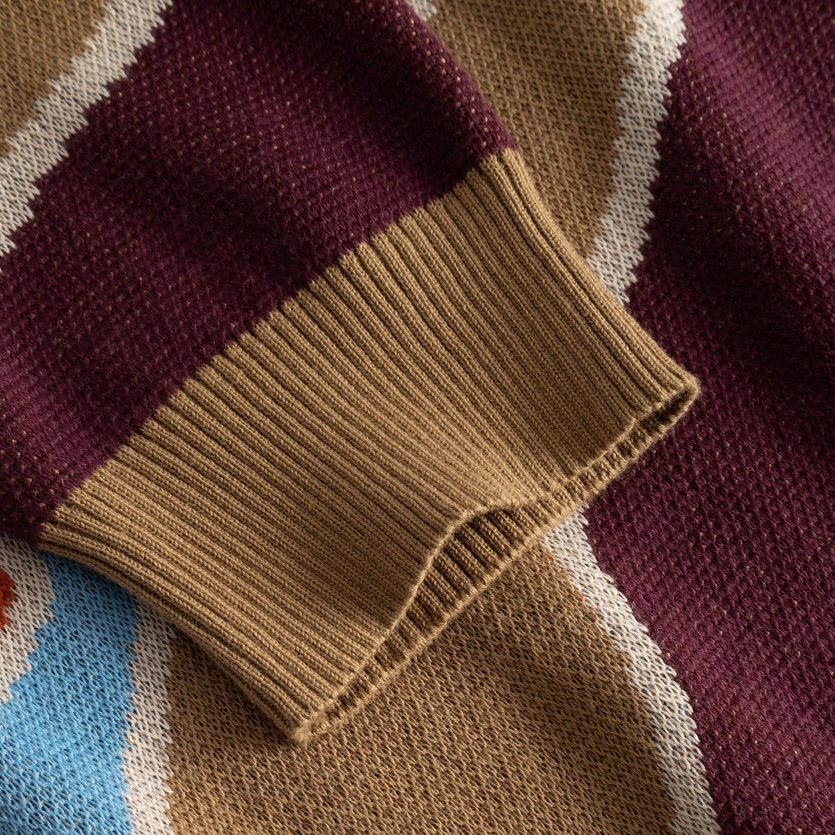 Close-up detail of the Mora Patch Valley sweater's ribbed cuff in tan, alongside the multi-colored jacquard knit.