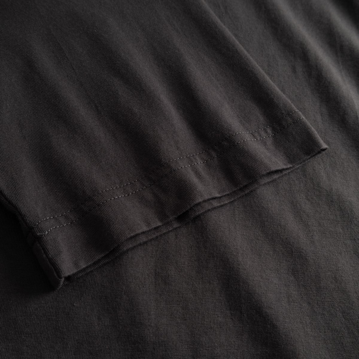 A close-up of the charcoal T-shirt Vadstena, highlighting the detailed stitching on the sleeve.