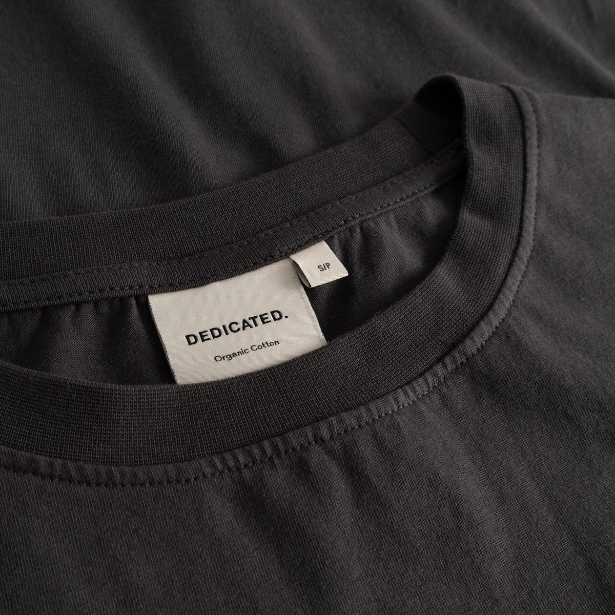 Detail shot of the Dedicated brand label inside the soft, ribbed collar of the charcoal T-shirt Vadstena.