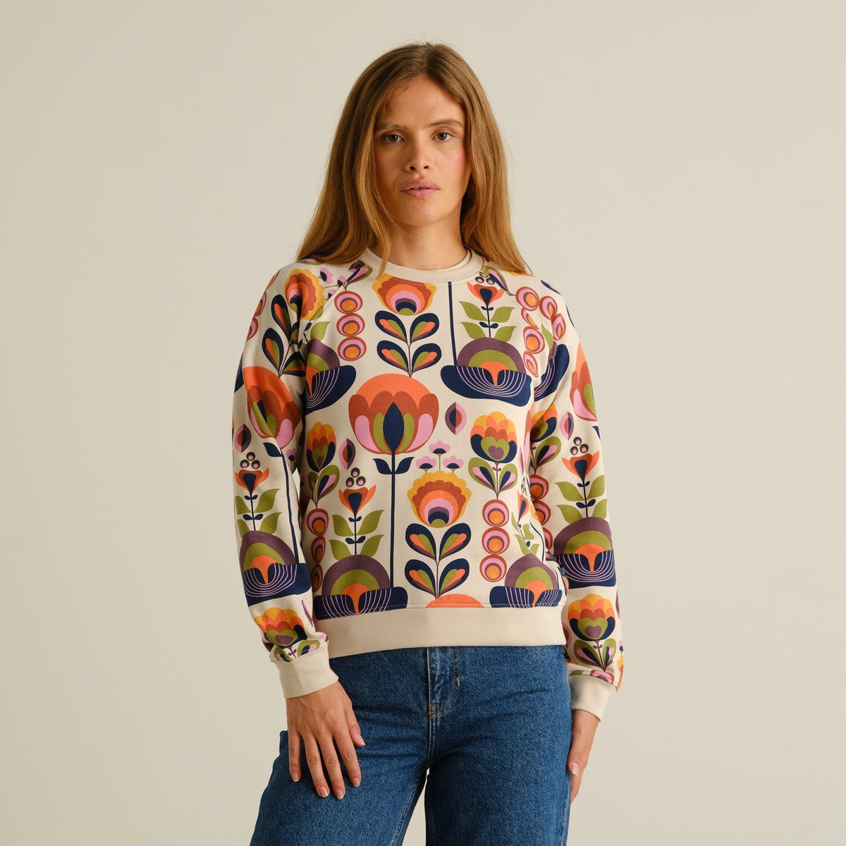 Front view of a woman wearing the vibrant, floral-printed Sweatshirt Ystad Autumn Harvest with classic blue jeans.