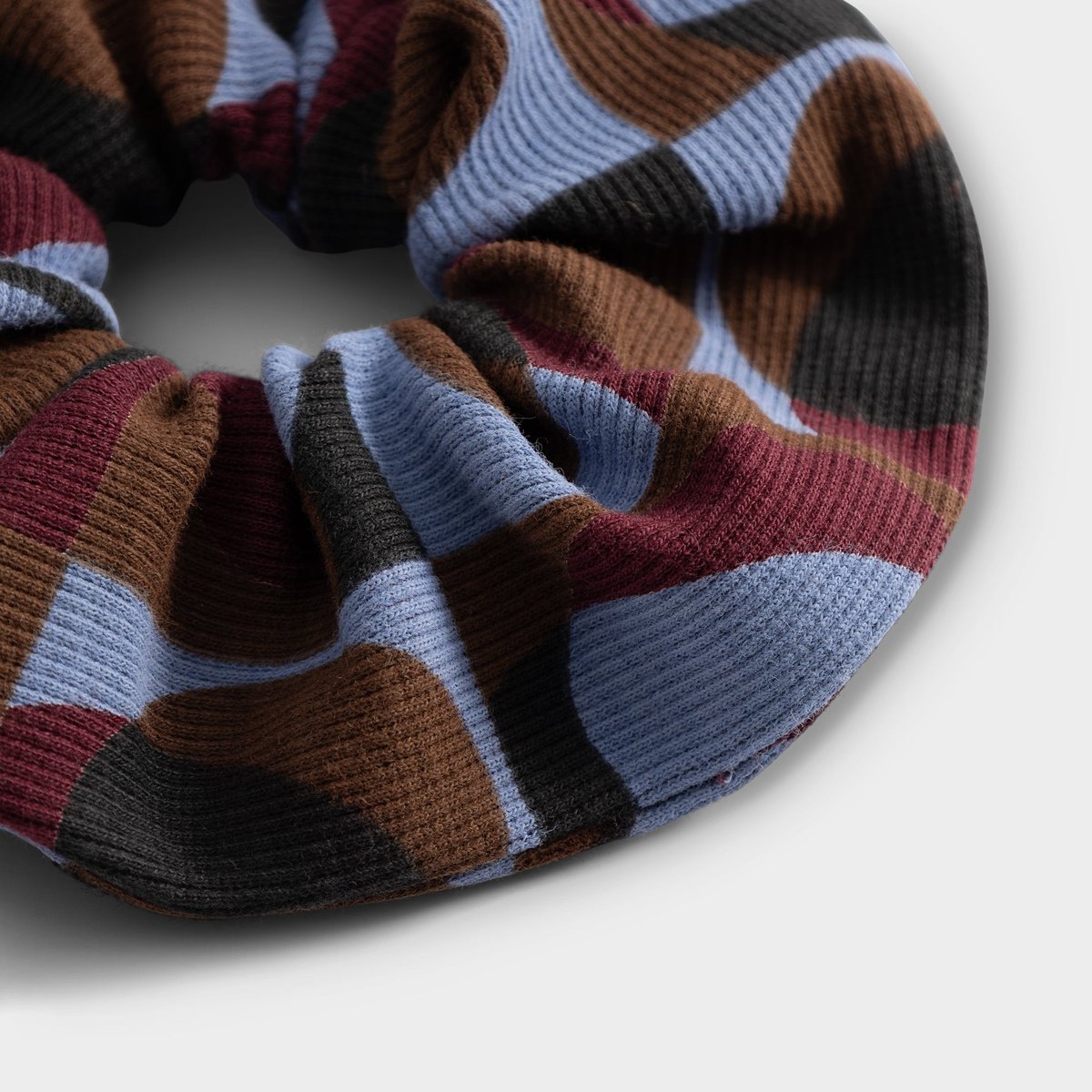 Nahaufnahme des gerippten Scrunchies mit einem geometrischen Retro-Muster in Blau-, Braun- und Bordeauxrot.