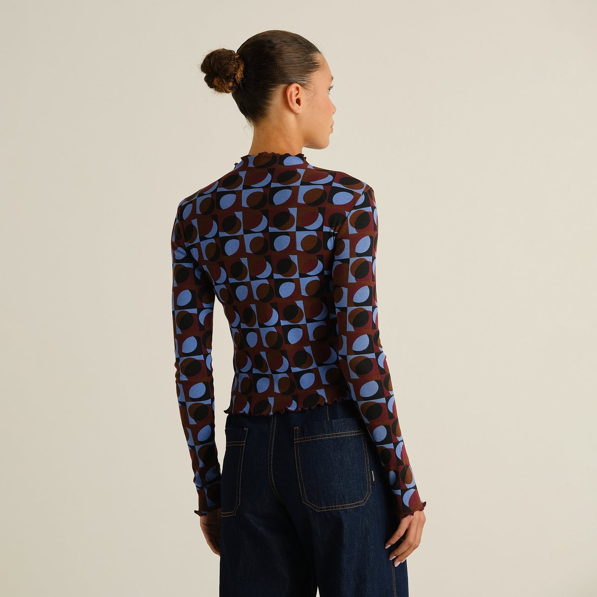 Model shown from the back wearing the long-sleeve Rib Top Ryd in a multi-colored retro geometric print with dark denim jeans.