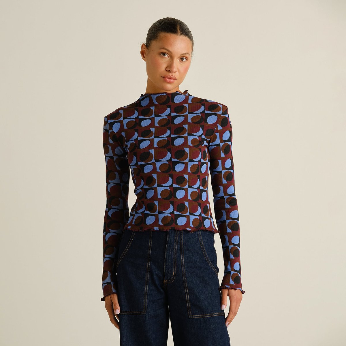 Model seen from the front wearing the long-sleeved Rib Top Ryd in a retro geometric print with dark denim jeans.