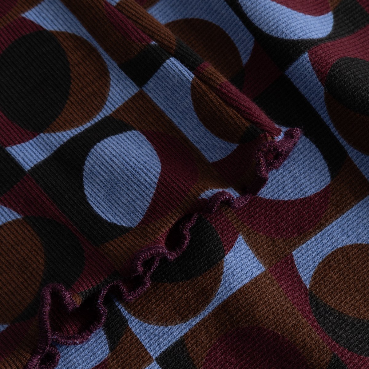 Close-up of the Rib Top Ryd, showing the colorful retro geo print, the soft ribbed fabric, and the wavy lettuce seam detail.