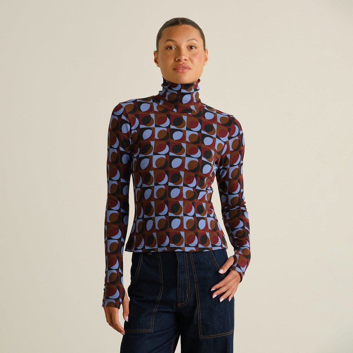 Front view of a model wearing the Rib Top Malma in a multi-color retro geo print, paired with dark denim jeans.