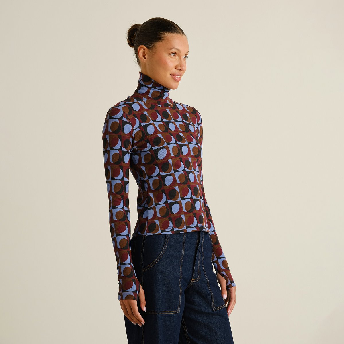 A smiling woman models the slim-fit Rib Top Malma in a fun Retro Geo Multi Color print, paired with dark wash jeans.