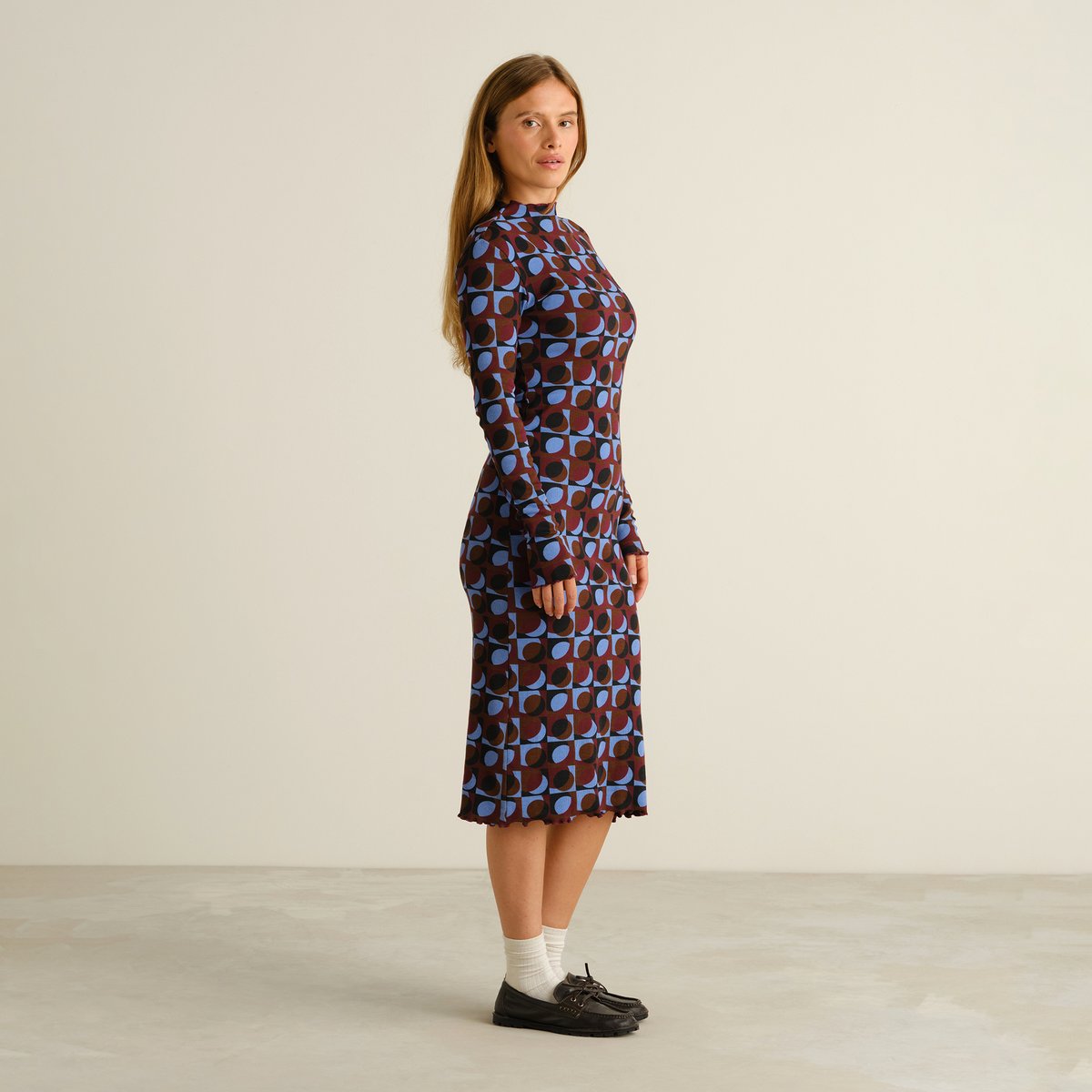Side profile of a woman wearing the long-sleeved Rib Dress Lofta in a colorful Retro Geo print, styled with loafers.