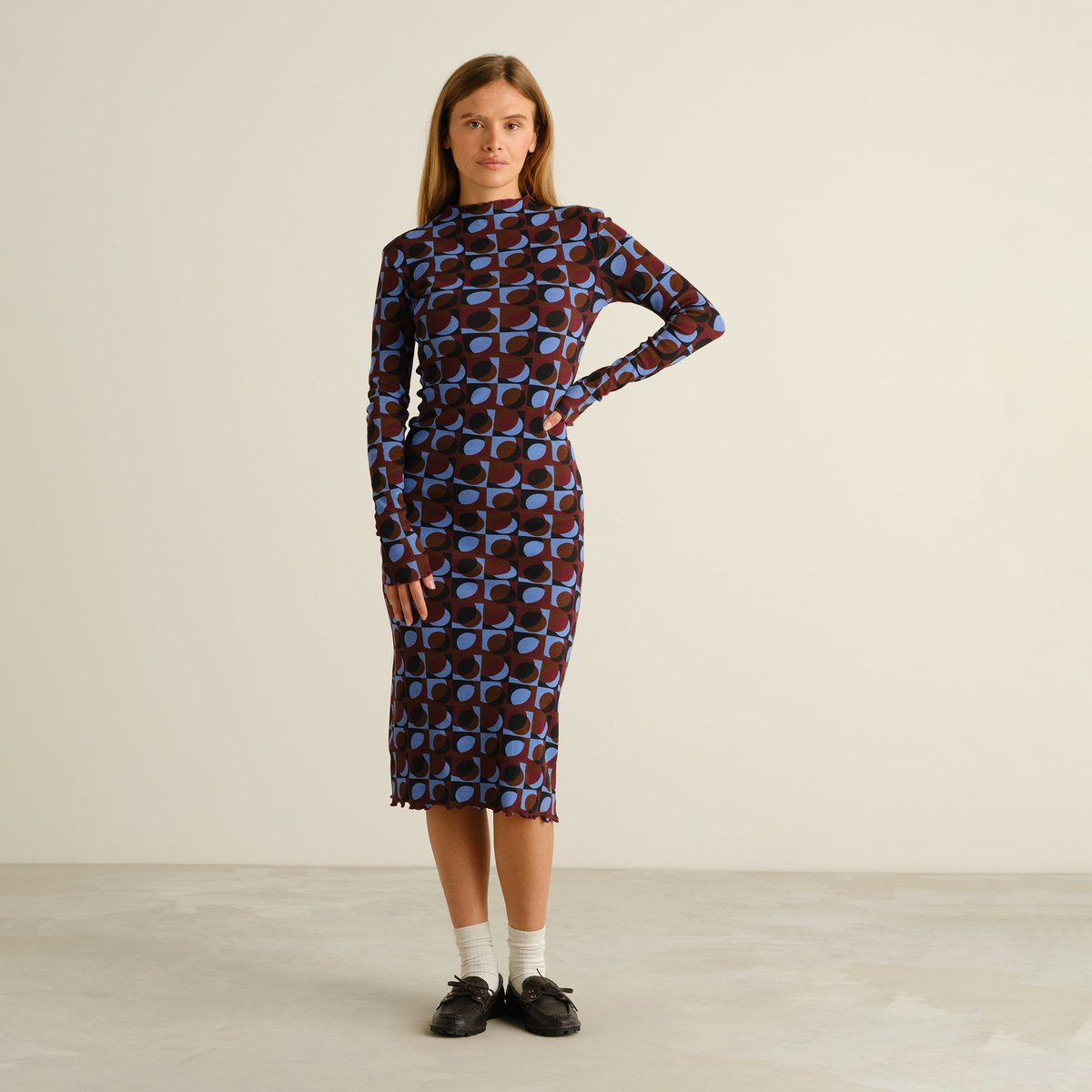 A model wears the Rib Dress Lofta, a long-sleeved midi dress featuring a bold Retro Geo print in shades of blue and brown.