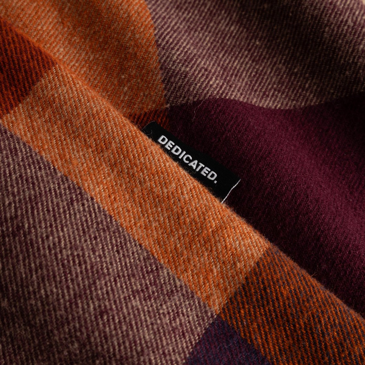 Close-up of the Rute Flannel Shirt's soft, brushed fabric in a muted multi-color check, showing the Dedicated logo tag.