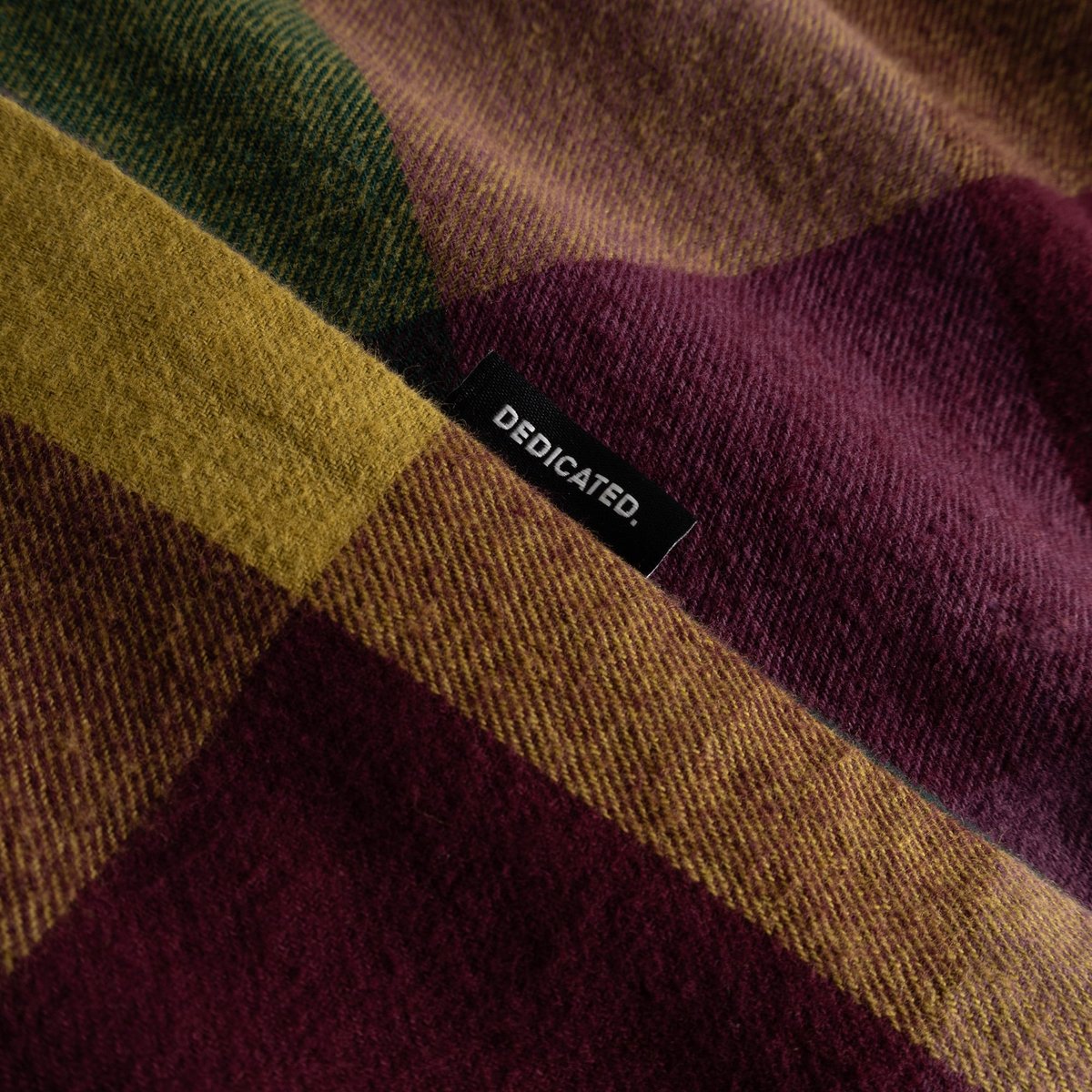 Close-up of the Shirt Rute Flannel's bold multicolor check pattern, showing the soft, brushed fabric and Dedicated brand tab.