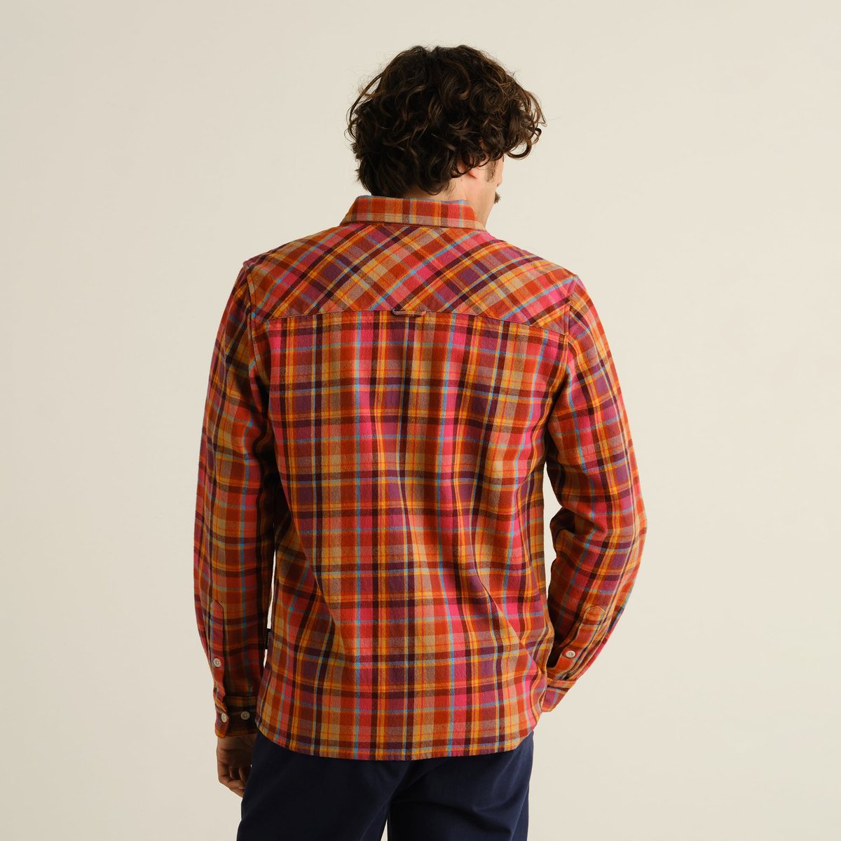 A man seen from behind wearing the relaxed-fit Rute Flannel Shirt in a vibrant multi-colored Madras check pattern.