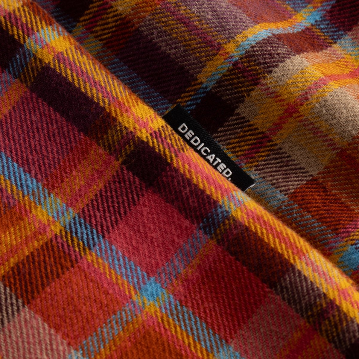 A close-up of Shirt Rute's soft, brushed flannel in a colorful Madras check pattern with the Dedicated logo tab.