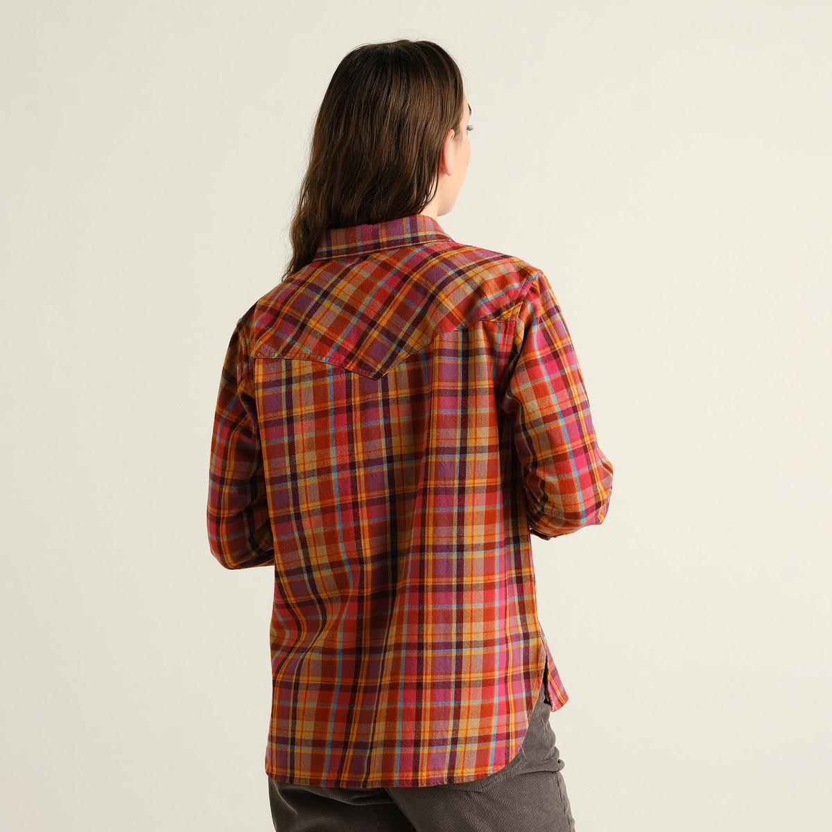 A woman seen from the back wearing the Arboga Flannel Shirt in a vibrant madras check pattern against a studio background.