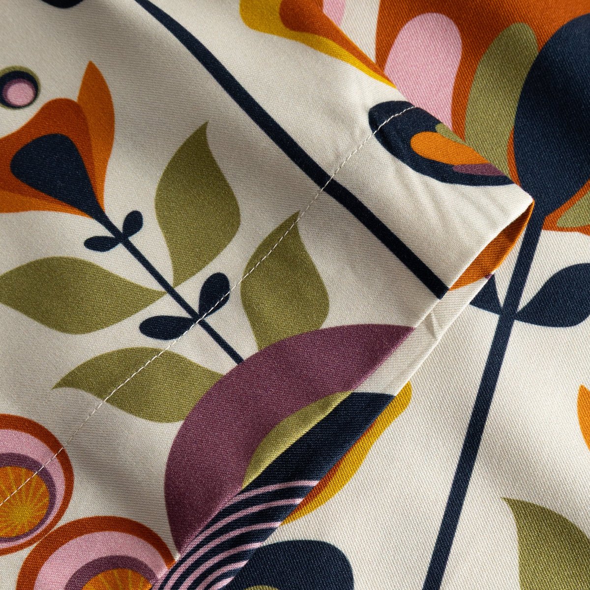A close-up of the Udda Top's Autumn Harvest print, featuring stylized flowers in rich oranges, pinks, and olive greens.