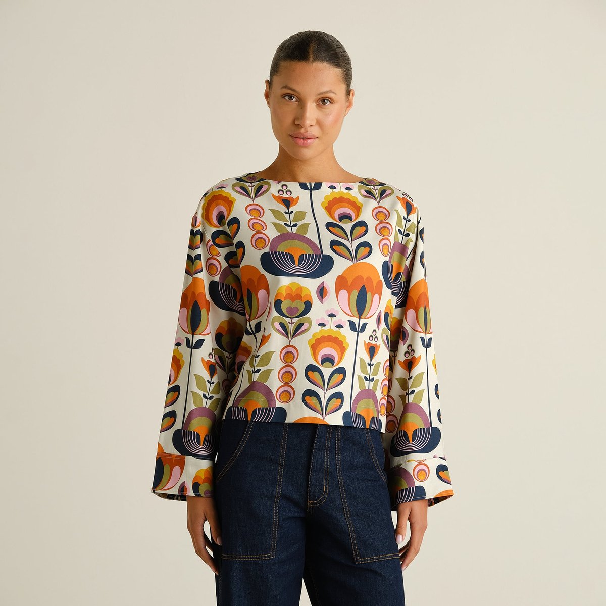 A model wears the modern, boxy Top Udda in a colorful Autumn Harvest print, featuring a boat neckline and wide sleeves.