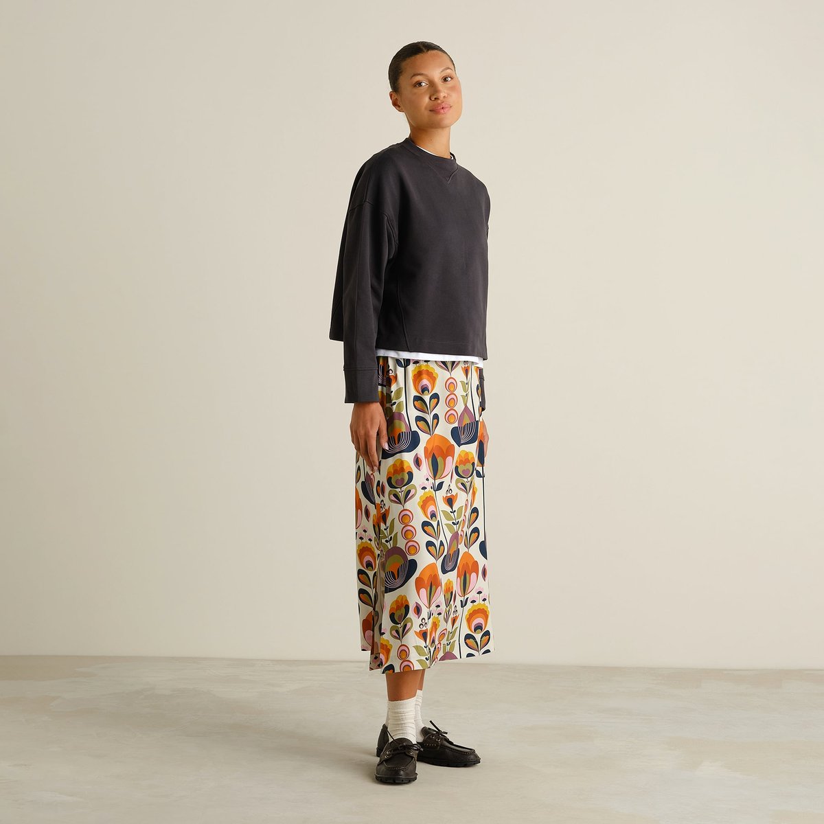 Side view of a model wearing the Skirt Viken Autumn Harvest, styled with a dark sweatshirt, white socks and black loafers.