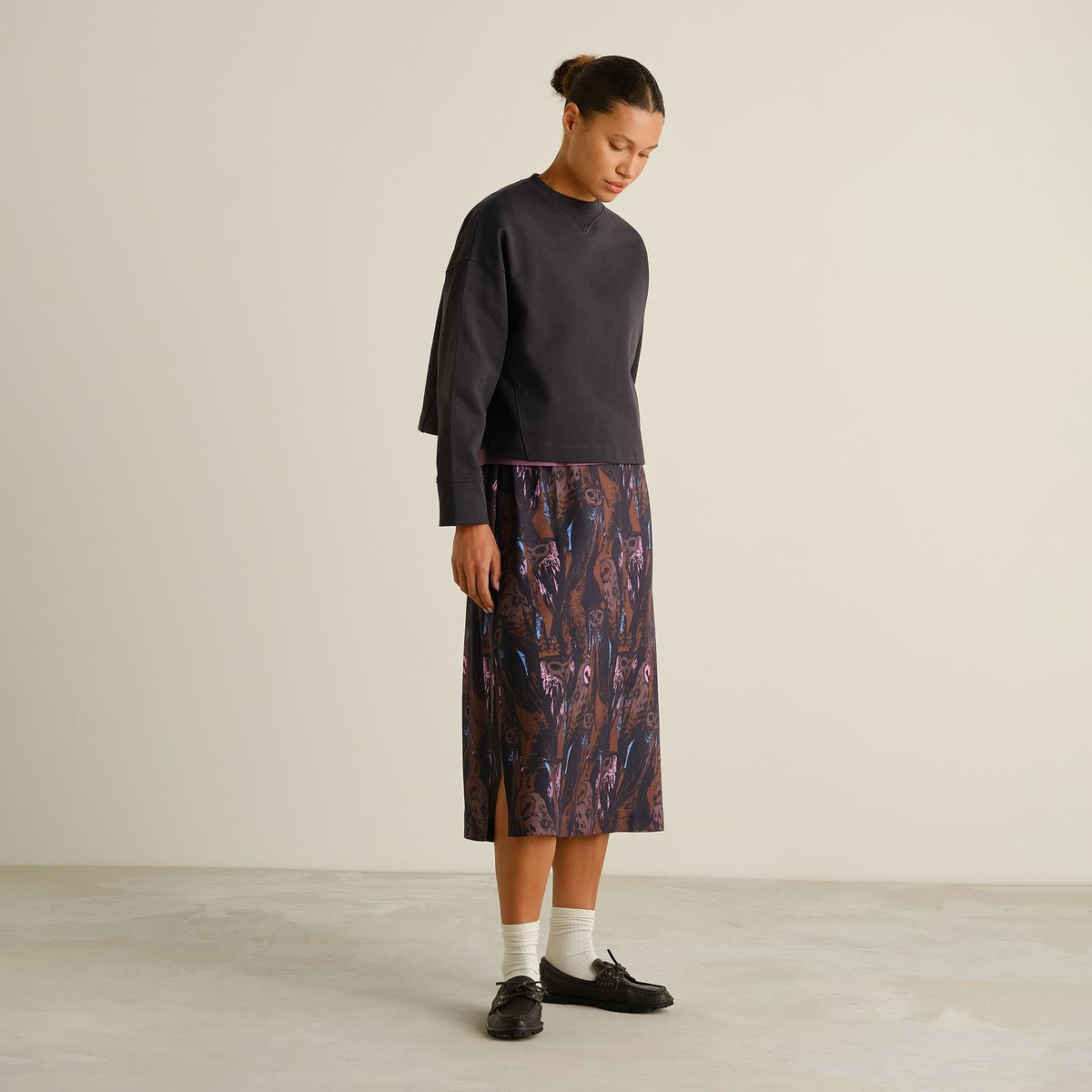 Model seen from the side wearing the Skirt Viken Owls Multi Color with a dark grey sweatshirt, white socks, & black loafers.