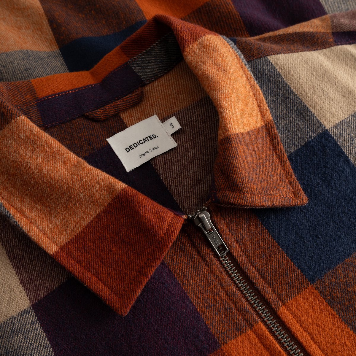 A detailed close-up of the Torp Flannel Check Jacket, showing the soft fabric, zipper, and the Dedicated brand label.