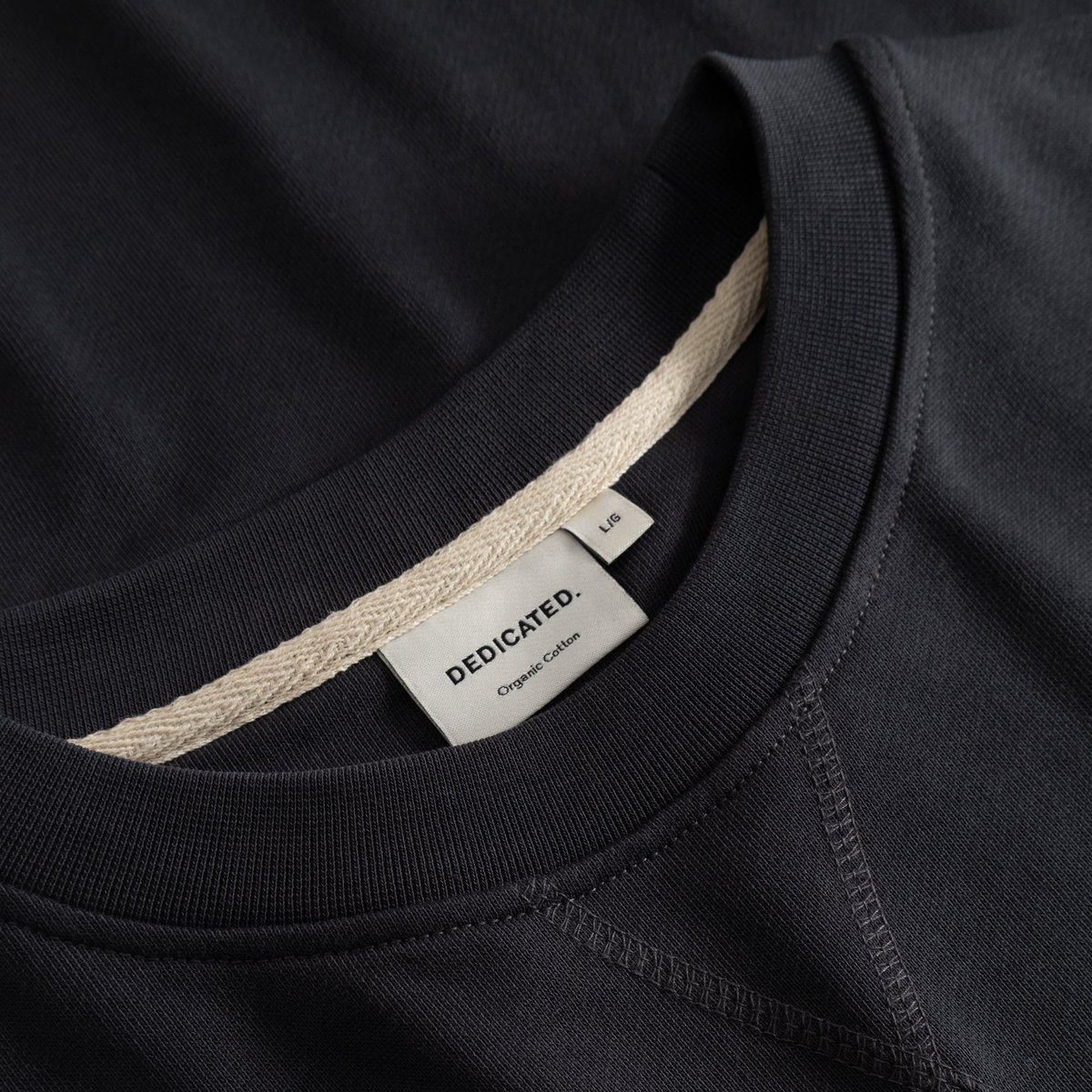 A close-up view of the Sweatshirt Bettna Phantom Black, highlighting the ribbed crew neck and classic Dedicated brand label.