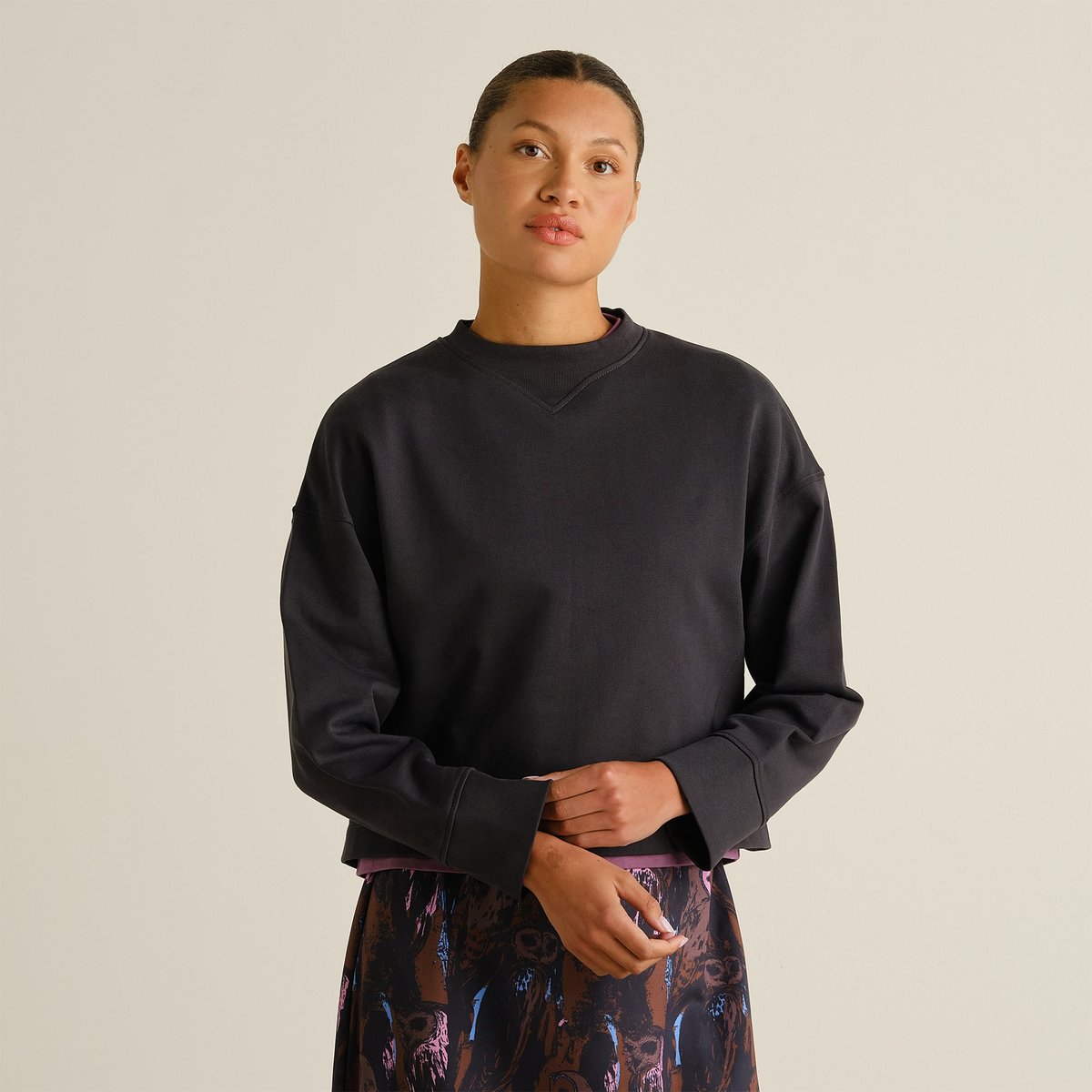 A model shows off the relaxed fit of the Sweatshirt Gia in Phantom Black, styled with a patterned skirt.