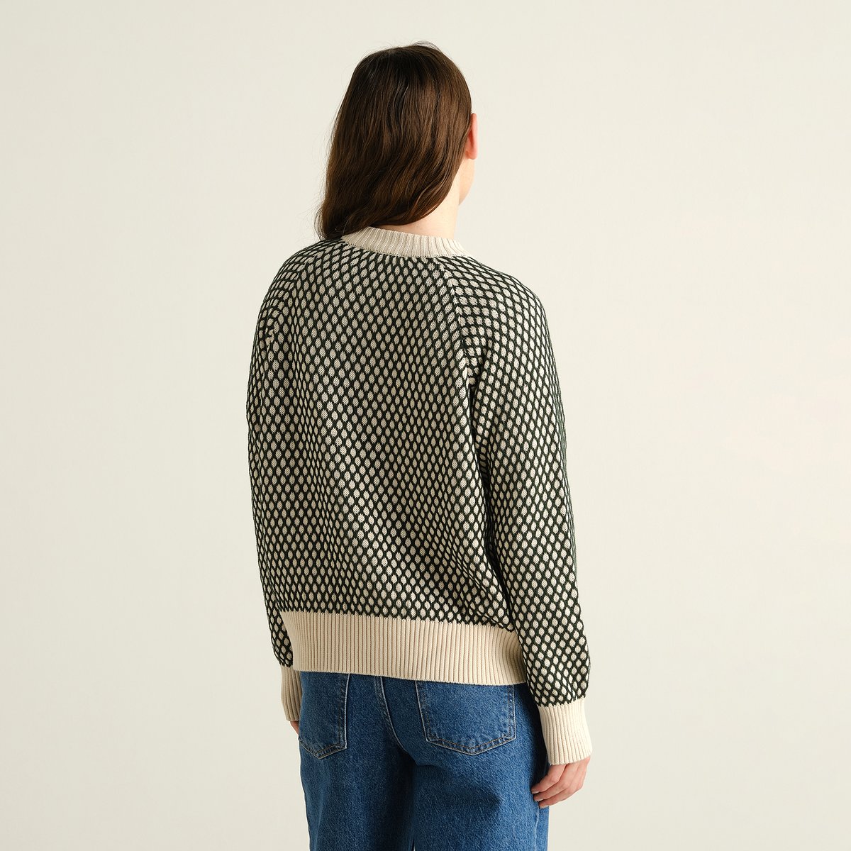 Bakifrån av en modell som bär den mönstrade tröjan Husie Bubble Knit i mörkgrönt och vaniljvitt med blå jeans.