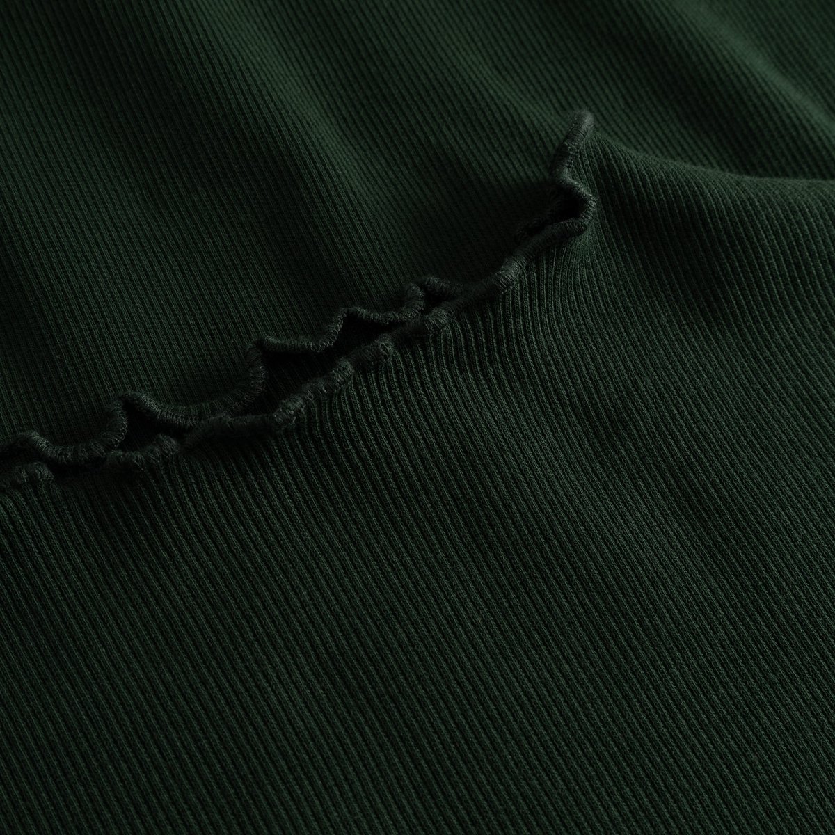 Close-up detail shot of the Rib Dress Lofta in dark green, showing the soft ribbed fabric and delicate lettuce seam.