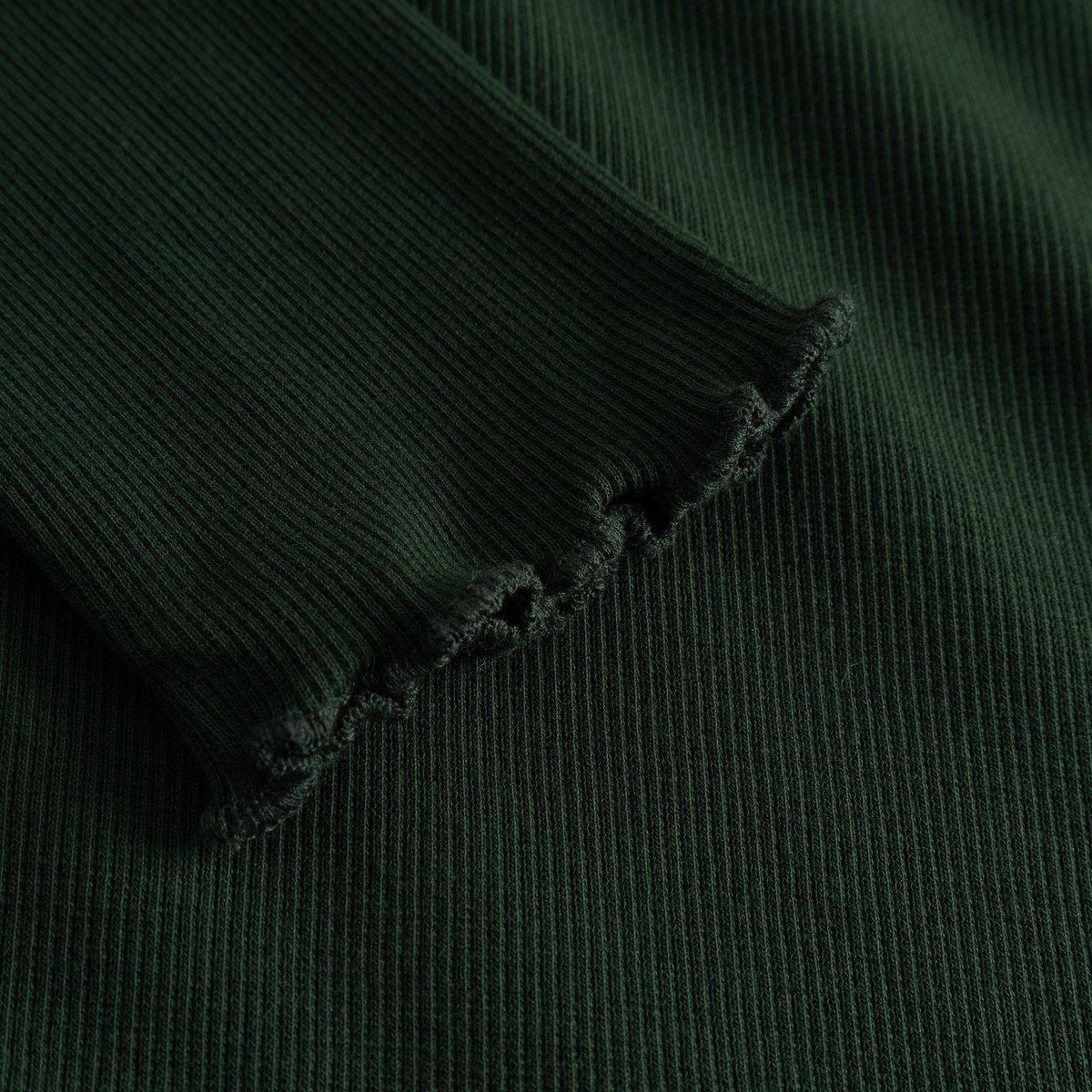A close-up view of the Rib Dress Lofta in dark green, highlighting the soft ribbed fabric and delicate lettuce-edge sleeve.